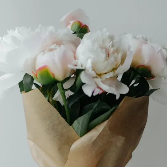 A wrapped peony bouquet carried upright by hand for same-day florist delivery